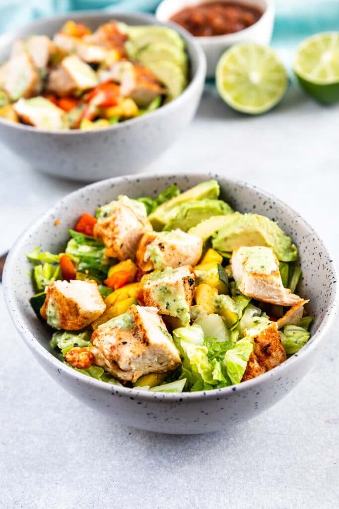 Two low carb grilled chicken power bowls with salsa and limes in background