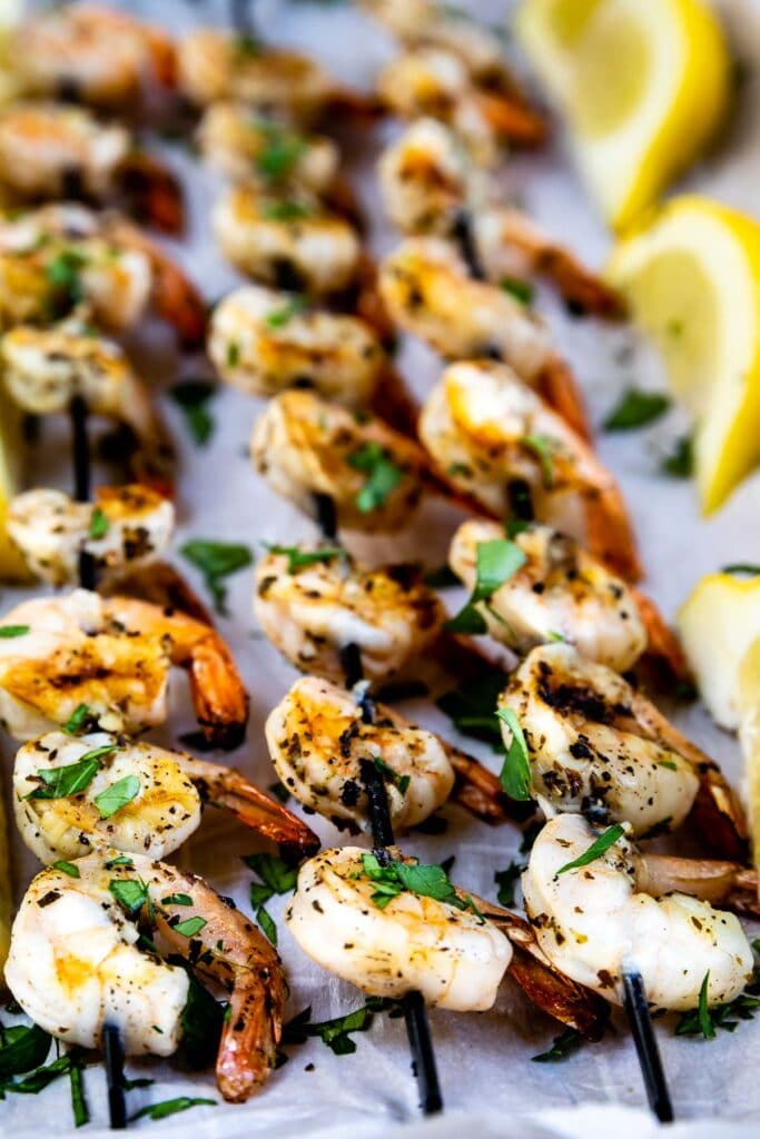 Three skewers of shrimp kabobs surrounded by lemons