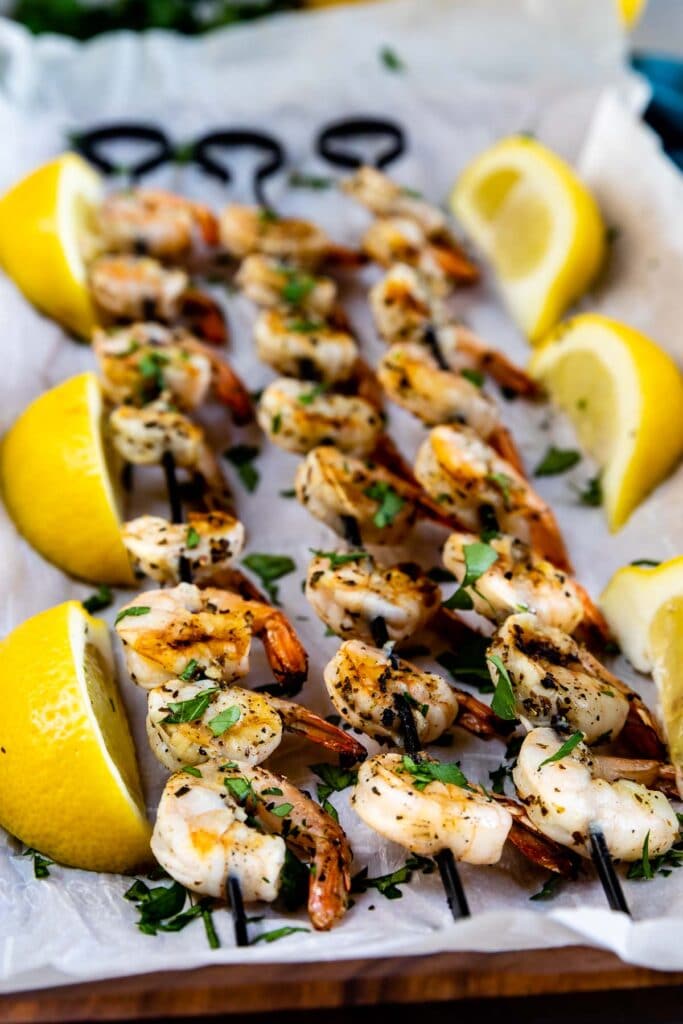 Three skewers of shrimp kabobs surrounded by lemons