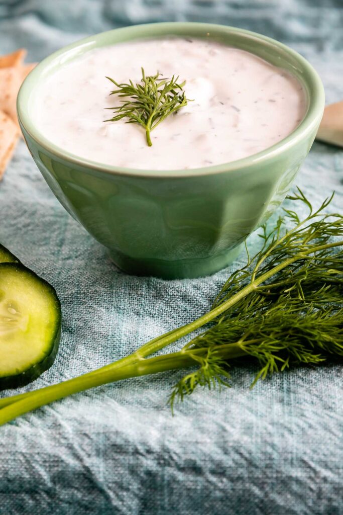 Tzatziki sauce with dill on top and ingredients and dippers around it