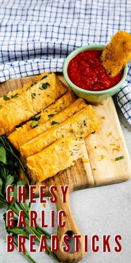 Cheesy Garlic Breadsticks on a cutting board with marinara sauce and recipe title on bottom of photo