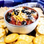 Crockpot pizza dip in a small bowl topped with cheese and olives and surrounded by crackers for dipping