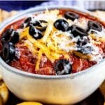 Crockpot pizza dip in a small bowl topped with cheese and olives and surrounded by crackers for dipping with recipe title on top of photo