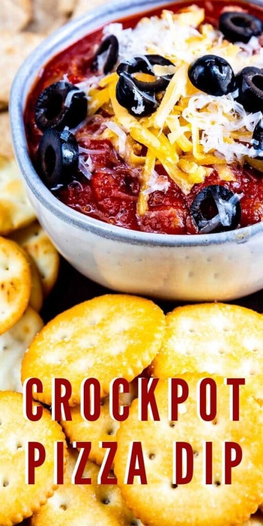 Crockpot pizza dip in a small bowl topped with cheese and olives and surrounded by crackers for dipping with recipe title on bottom of photo