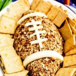 Overhead shot of Football Cheese Ball on a serving plate surrounded by crackers with recipe title on top of image