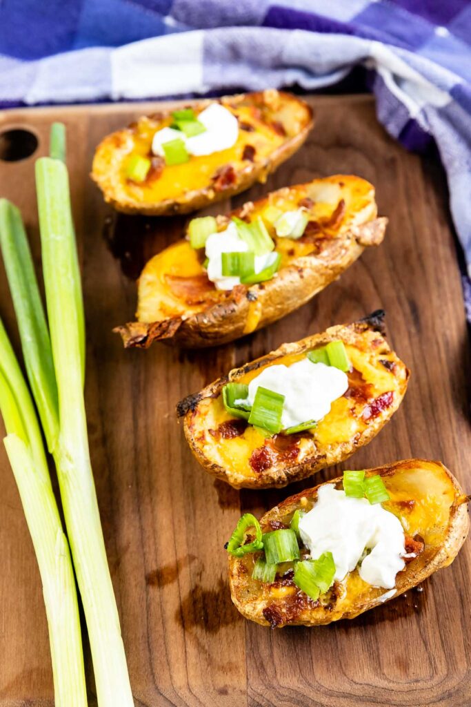 Four potato skins on a wooden cutting board next to green onions