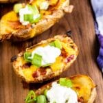 Overhead close up shot of four loaded potato skin on a wooden cutting board