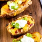 Overhead close up shot of four loaded potato skin on a wooden cutting board with recipe title on bottom of photo