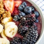 Close up overhead shot of acai bowl with honey in background and recipe title on bottom of photo