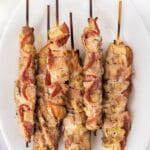 Overhead shot of chicken bacon skewers on a plate with recipe title on top of image