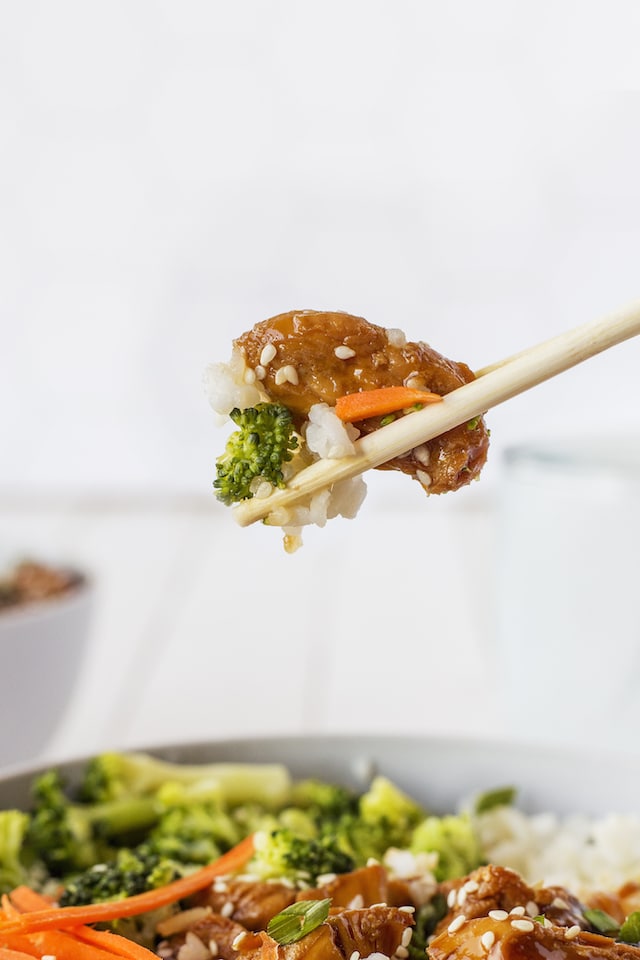 Close up shot of one bite of chicken teriyaki bowl on a chopstick