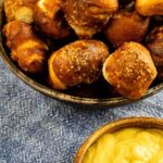 Close up overhead shot of air fryer pretzel bites in a serving bowl next to honey mustard and recipe title on bottom of photo