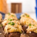 Crab stuffed mushrooms on wooden cutting board with recipe title on top of image