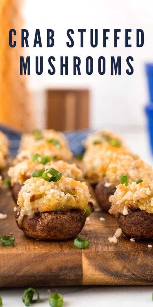 Crab stuffed mushrooms on wooden cutting board with recipe title on top of image