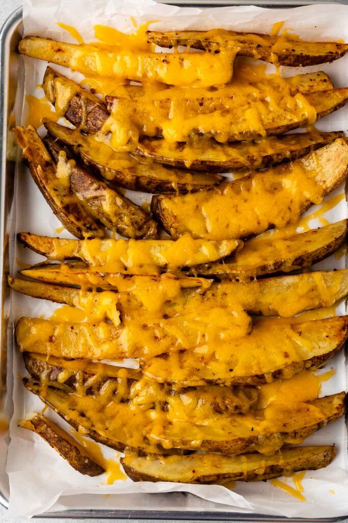 Overhead shot of potato wedges covered in melted cheese on a sheet pan