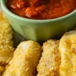 Close up shot of air fryer mozzarella sticks next to a small bowl of marinara sauce and recipe title on top of image
