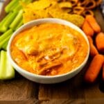 Buffalo chicken dip in a small bowl surrounded by chips, pretzels, carrots and celery