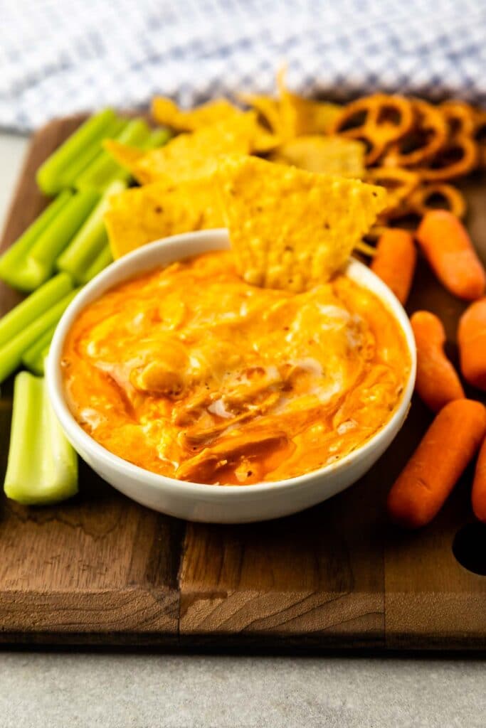 Buffalo chicken dip in a small bowl surrounded by chips, pretzels, carrots and celery