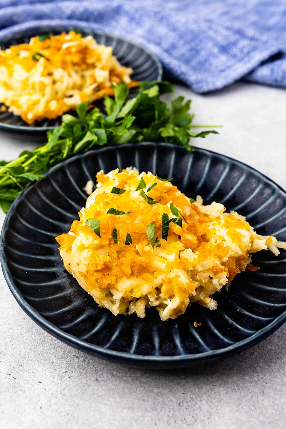 Two plates of hash brown casserole with herbs in between them