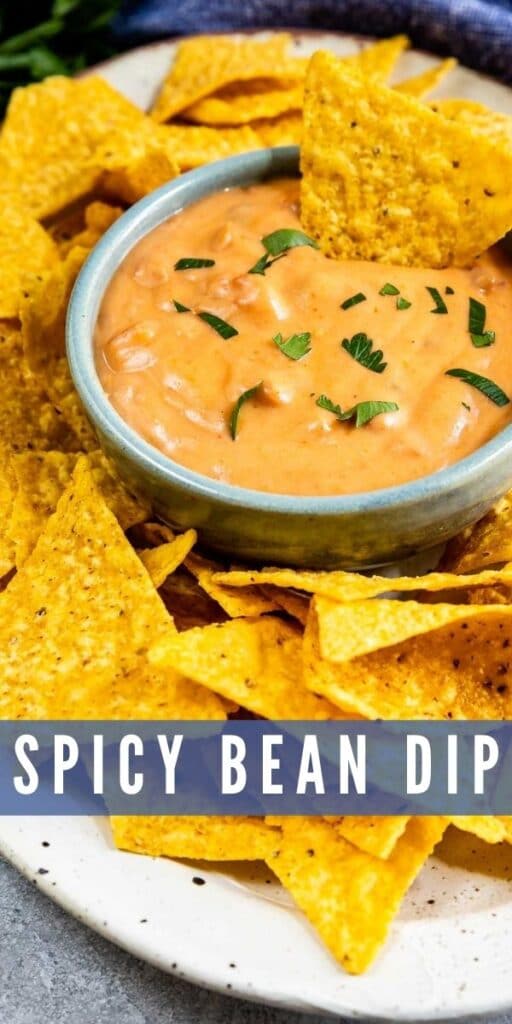 One chip being dipped into spicy bean dip with more all around the dip with recipe title on bottom of photo