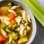 Close up overhead shot of a bowl of chicken vegetable soup next to celery stalks