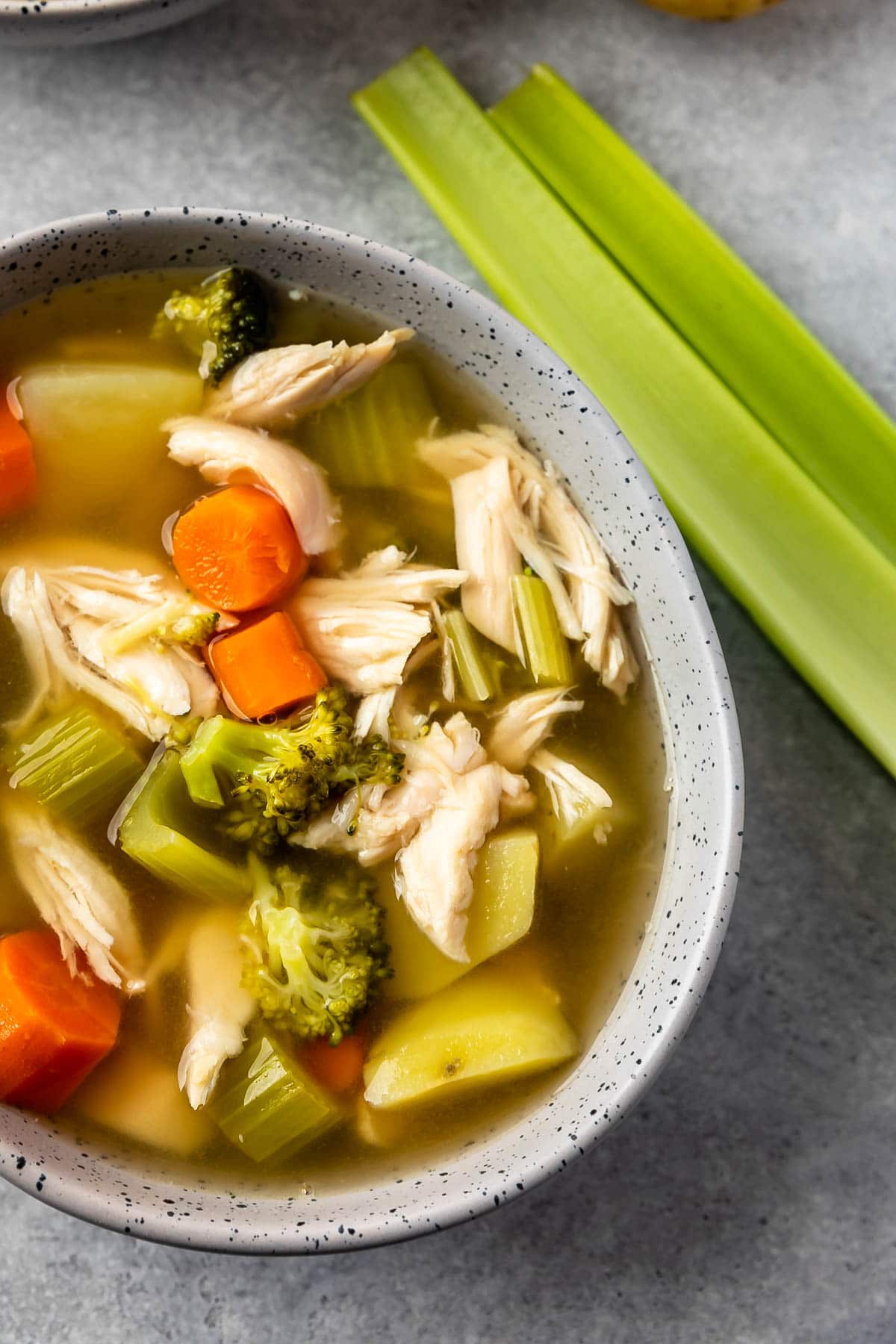 Close up overhead shot of a bowl of chicken vegetable soup next to celery stalks