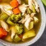 Close up overhead shot of a bowl of chicken vegetable soup next to celery stalks and recipe title on bottom of image