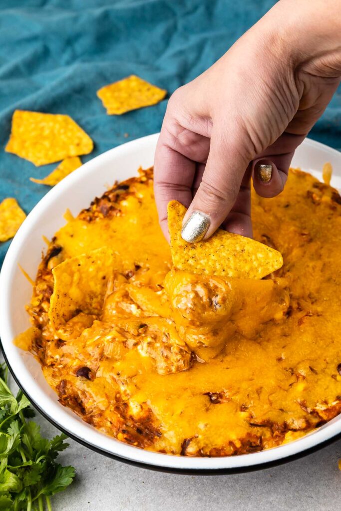 Hand dipping a chip into the chili cheese dip