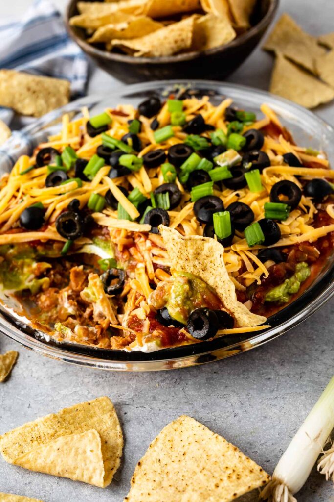 7 layer dip in a glass casserole dish with tortilla chips behind it