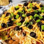7 layer dip in a glass casserole dish with tortilla chips behind it with the recipe title on bottom of image