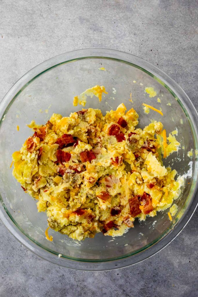 Overhead shot of cheese and bacon smashed potatoes in glass bowl