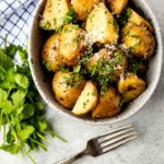 Crockpot garlic herb potatoes in a serving bowl topped with parmesan cheese and parsley