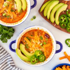 Overhead shot of taco soup in small bowls topped with avocado, jalapeno and tortilla strips