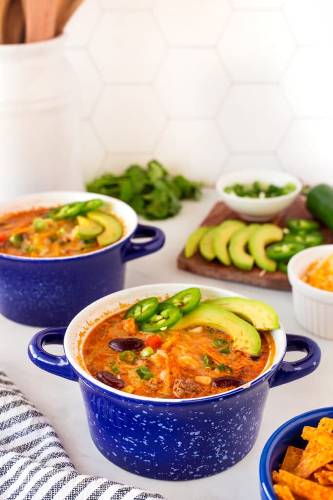 Taco soup in small bowls topped with avocado, jalapeno and tortilla strips
