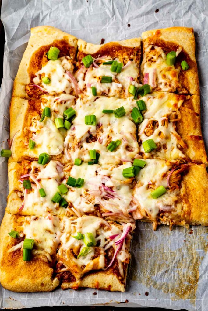 Overhead shot of bbq chicken pizza cut into squares with bottom right square missing