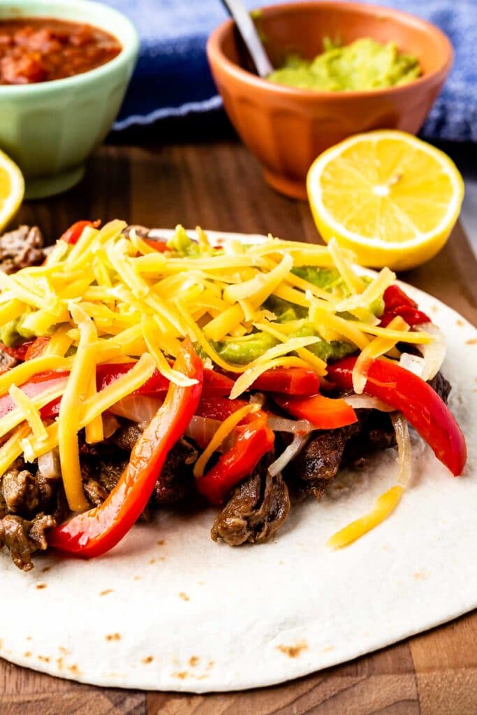 Close up shot of a steak fajita topped with peppers, onions, cheese and guacamole