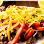 Close up shot of a steak fajita topped with peppers, onions, cheese and guacamole with recipe title on top of image
