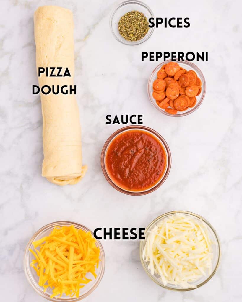 Top-down view of pizza ingredients on a marble surface: rolled pizza dough, a small bowl of spices, a bowl of sliced pepperoni, tomato sauce, shredded cheese, and cheddar—perfect for crafting delectable pizza rolls. Each item is neatly labeled.