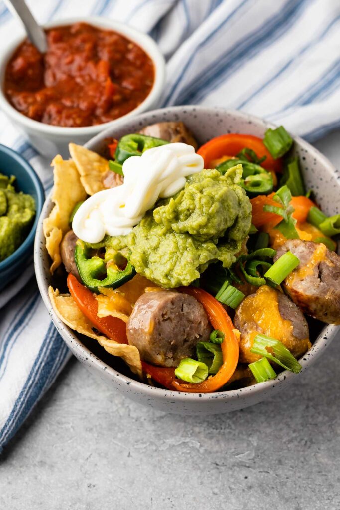 Bowl full of bratchos topped with sour cream and guacamole