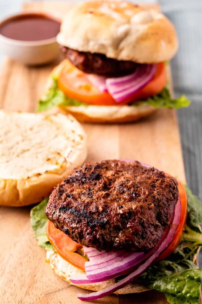 Cola burgers with on a cutting board. One burger has the top half of the bun laying upside down on the cutting board