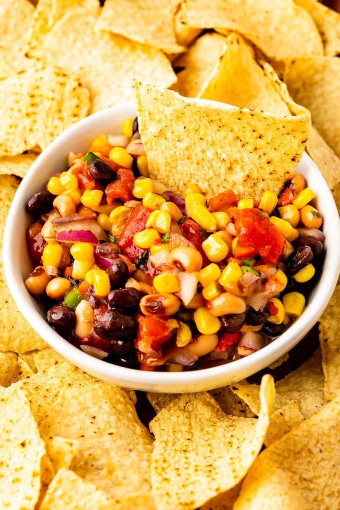 A white bowl of cowboy caviar surrounded by tortilla chips