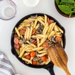 Mushroom and spinach pasta in a cast iron skillet with ingredients behind it in small bowls