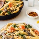 collage of mushroom and spinach pasta on a white plate with a skillet of pasta in the background