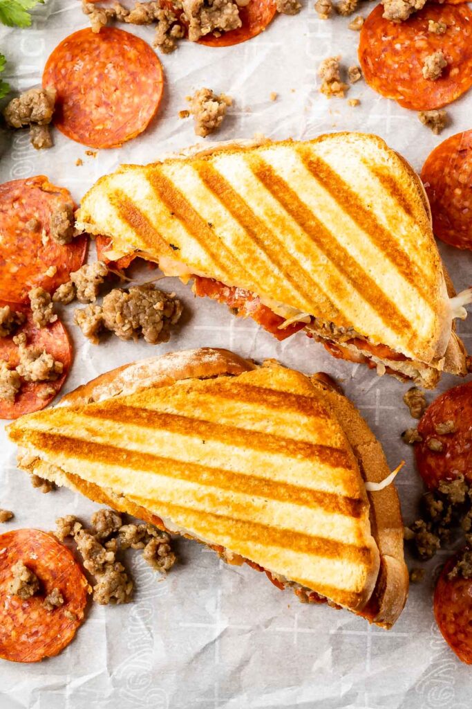 overhead shot of two halves of pizza panini sandwich with pepperoni and sausage scattered on a table