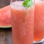 watermelon drink in a tall clear glass with a green straw and green garnish.