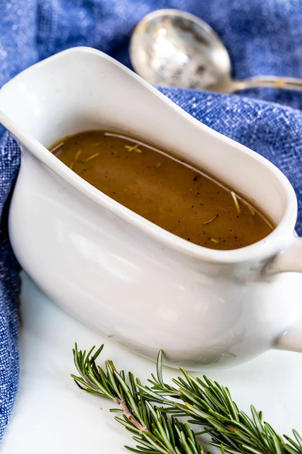 gravy in white gravy boat with rosemary and blue napkin.