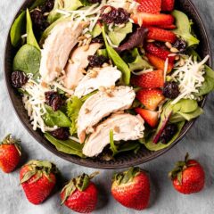 brown bowl with strawberry chicken salad and a row of uncut strawberries in front of the bowl