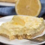 lemon square on white plate with fork and bite missing.