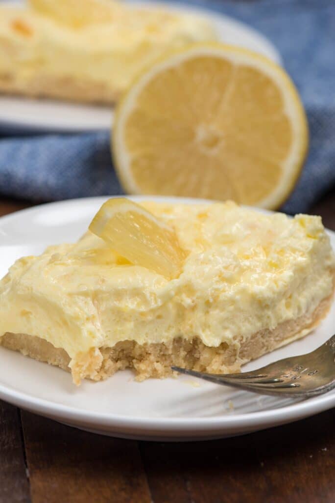 lemon square on white plate with fork and bite missing.