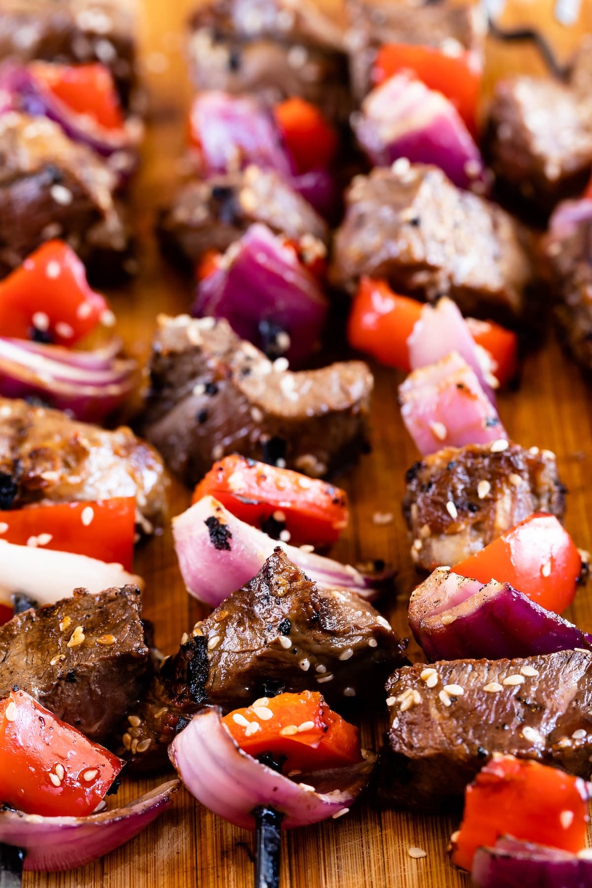 steak and peppers and onions shoved on top black skewers and laid on a wood cutting board.